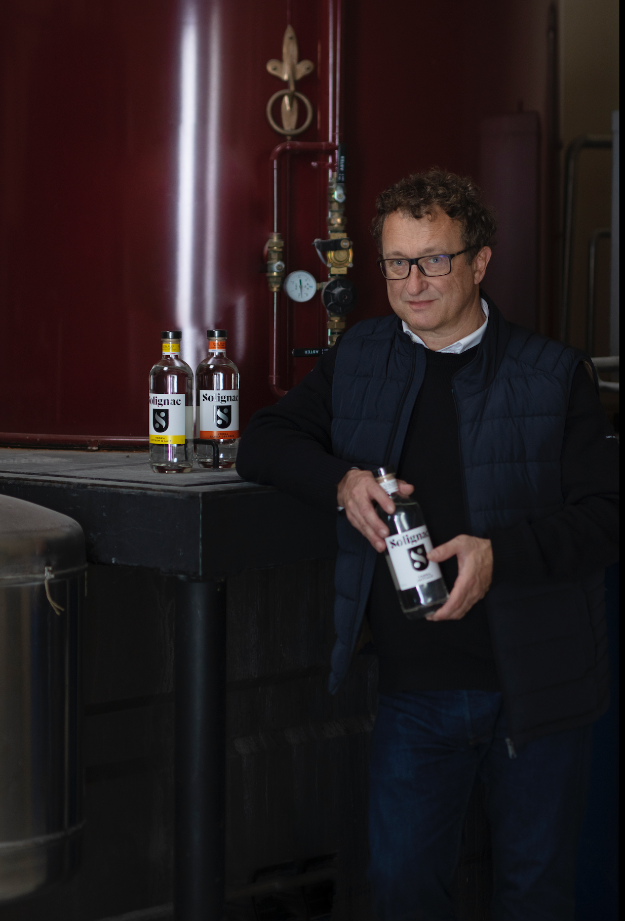 Pierre Solignac holding a bottle of Solignac initiale vodka in front of distillation 