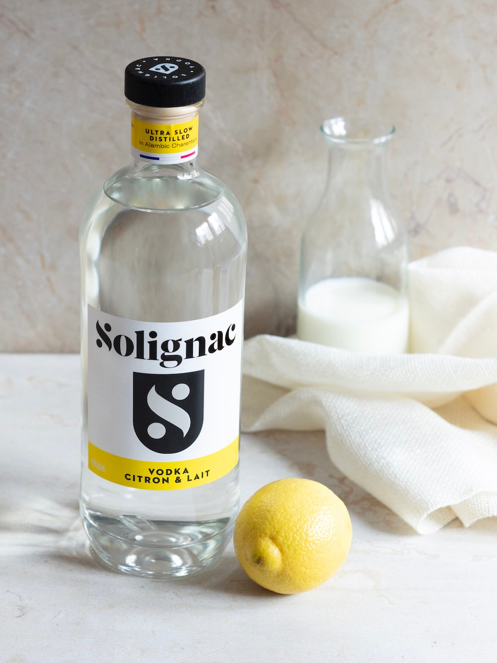 Bottle of Solignac vodka with a lemon on a light surface, Vodka citron lait by Maison Solignac